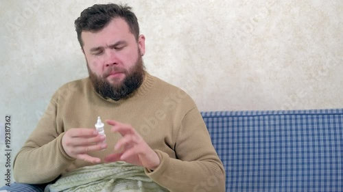 A man with a cold sits on the couch. He sprinkles a special nasal spray into his nose. photo