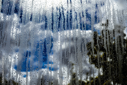 Glass window with rain, sky clouds and sun on background © Oksana