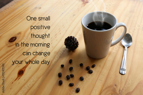 Inspirational positive quote “ One small positive thought in the morning can change your whole day.” with hot coffee with steam in a white cup and coffee bean on the wooden desk.