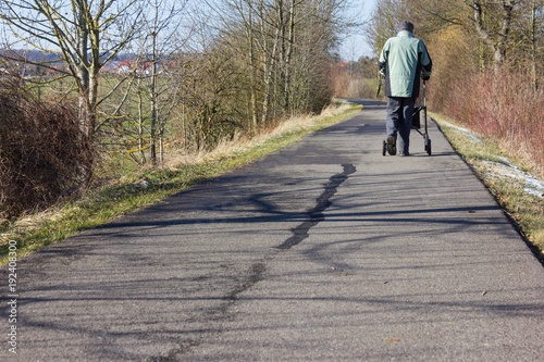 senior man with rollator on a bikeway and sunny winter day