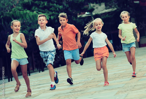 Fototapeta Naklejka Na Ścianę i Meble -  Group of cheerful children running together in town on summer