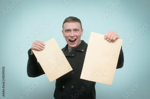 Happy amazed man is holding in hands a two wooden boards nameplates in gront of him and laughing isolated on blue background. photo