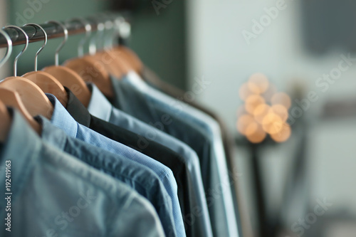 Clothes rack with many shirts indoors, closeup. Fashionable wardrobe