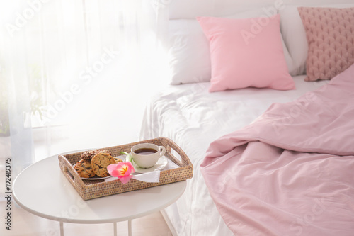 Tray with tasty breakfast and tulip on table near bed