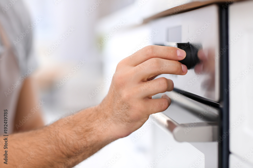 Man adjusting electric oven in kitchen, closeup Man adjusting electric oven in kitchen, closeup