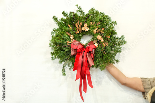 Female florist with Christmas wreath on light wall background