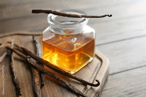 Jar with vanilla extract and sticks on wooden board