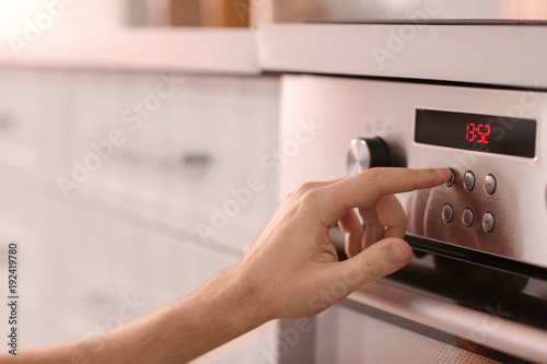 Man adjusting electric oven in kitchen, closeup