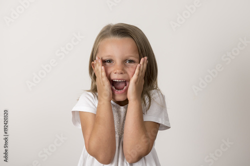 portrait of 7 years old sweet little girl with mouth open screaming surprised or scared holding his head with his small hands isolated on white background