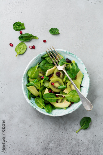Salad of spinach baby leaves, watercress, kiwi, avocado and pomegranate in old ceramic plate on gray concrete background. Selective focus. Top view. Copy space.