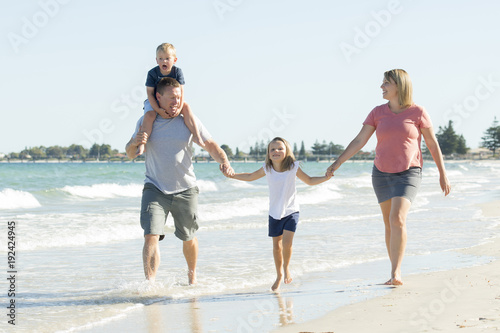 young happy and beautiful family mother father holding hand of son and daughter walking joyful on the beach enjoying Summer holidays