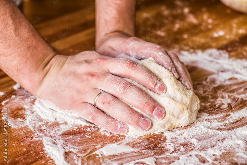 male hands kneading dough on wooden table