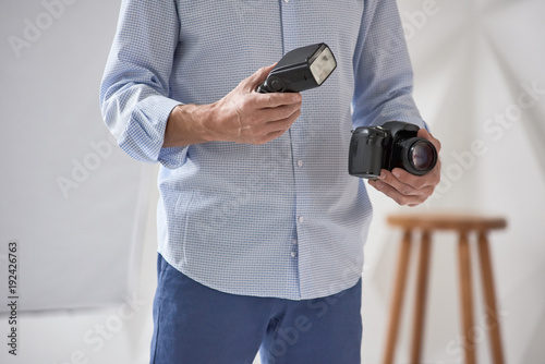 Man holding camera and flash. Closeup of young man holding digital camera with synchronizer and flash in studio, focus is on hand with flash photo