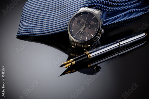 Father's Day or business concept image. Elegant man's watch, fountain pen and blue tie on black gradient background.