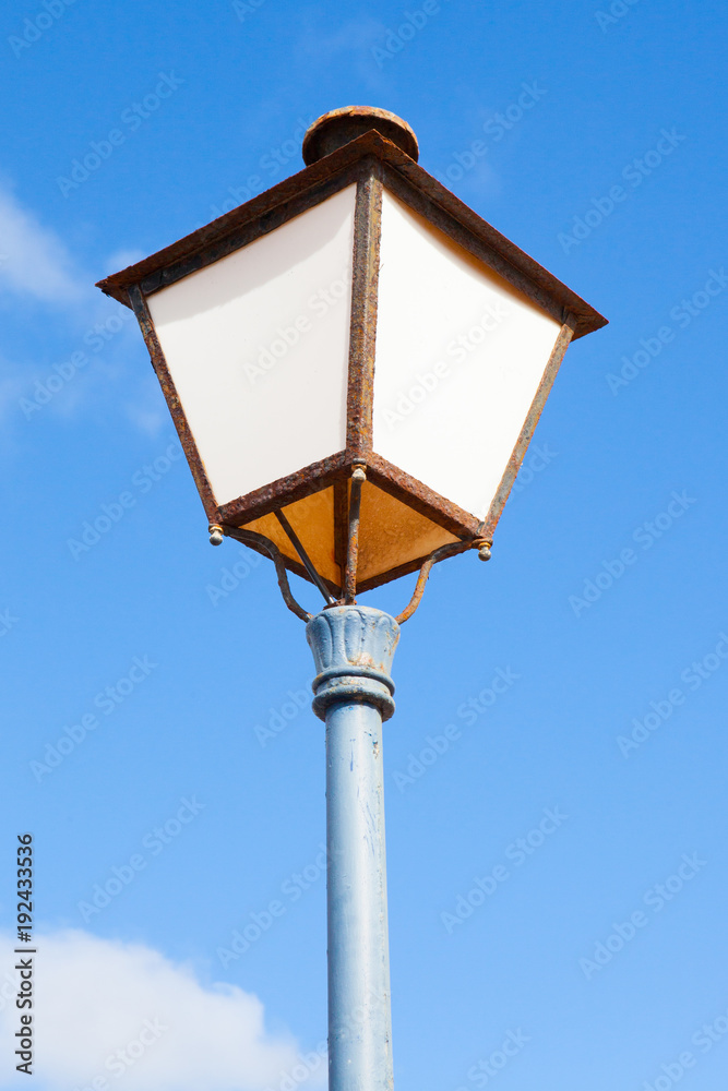 Detail of a rusted street lamp post with blue sky on the background Detail of a rusted street lamp post with blue sky on the background