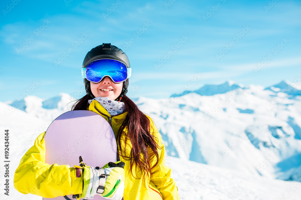 Photo of smiling brunette in helmet and mask with snowboard on background of snowy hills