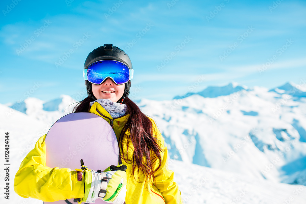 Photo of smiling brunette in helmet and mask with snowboard on background of snowy hills Photo of smiling brunette in helmet and mask with snowboard on background of snowy hills
