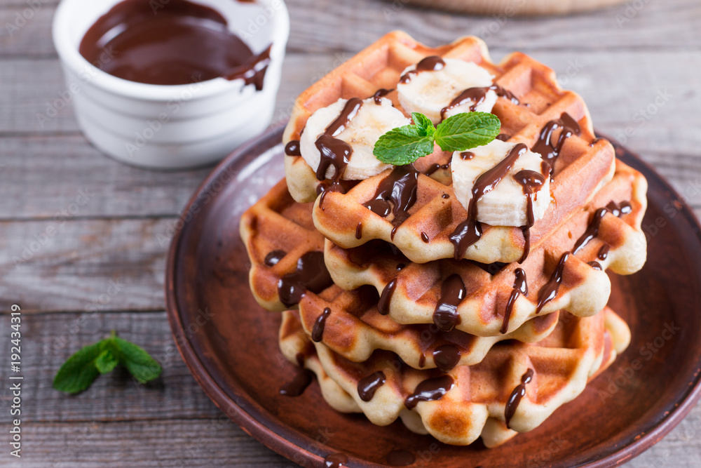 Belgian waffles with chocolate syrup and banana slice on a plate on a wooden background