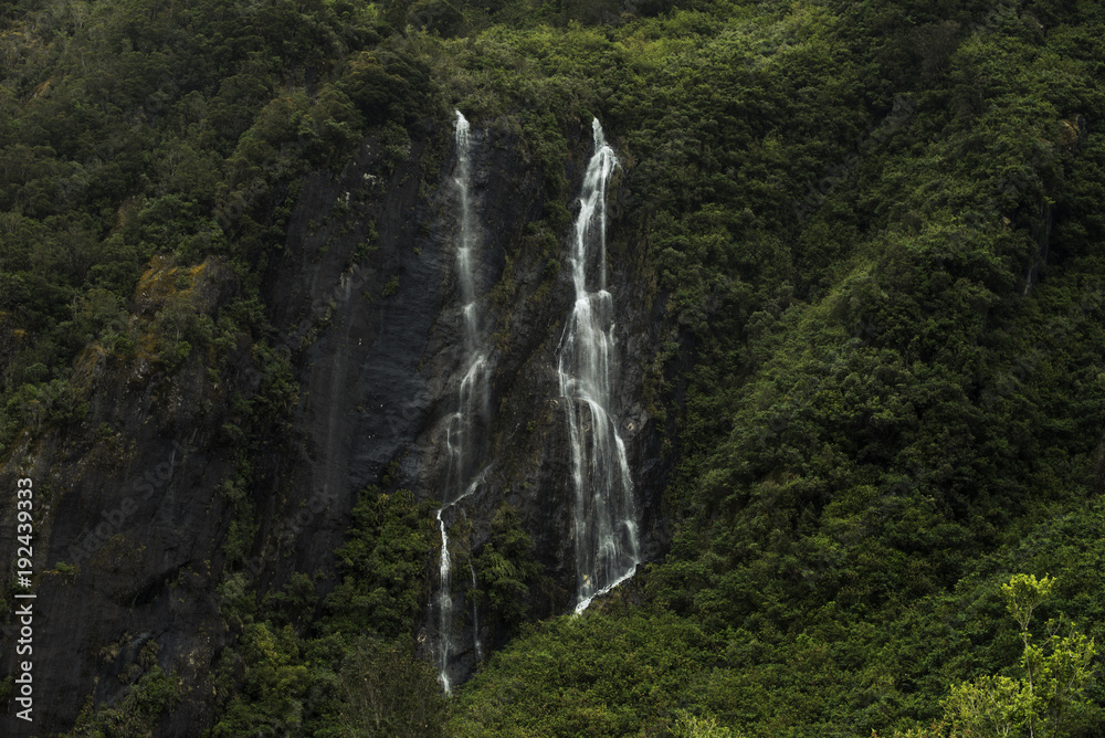 Doble cascada cayendo por la ladera de una montaña llena de vegetación Doble cascada cayendo por la ladera de una montaña llena de vegetación