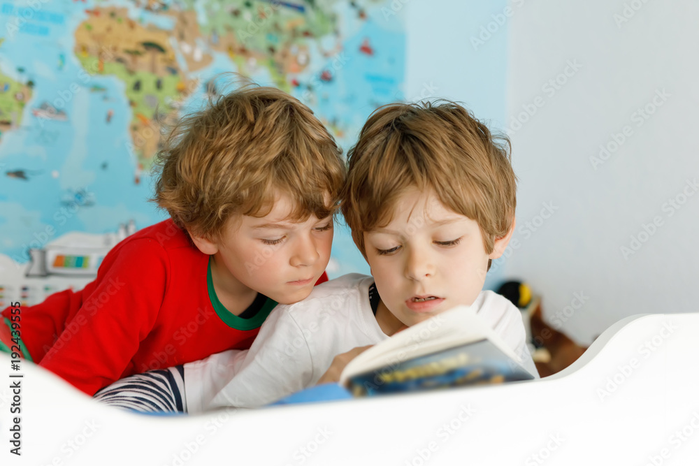 Two little kids boys in pajamas reading a book in bed. Two little kids boys in pajamas reading a book in bed.