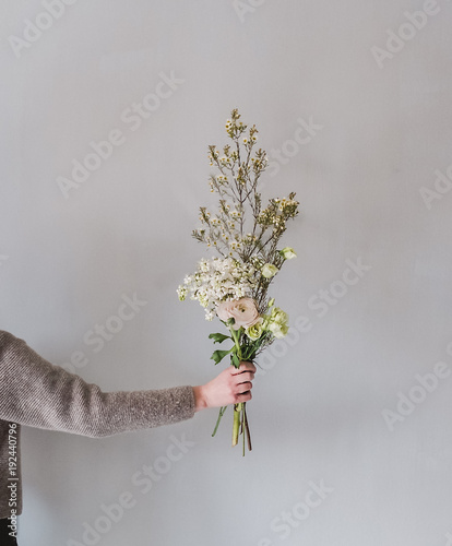 Woman's hand holding bouquet of flowers against gray wall
