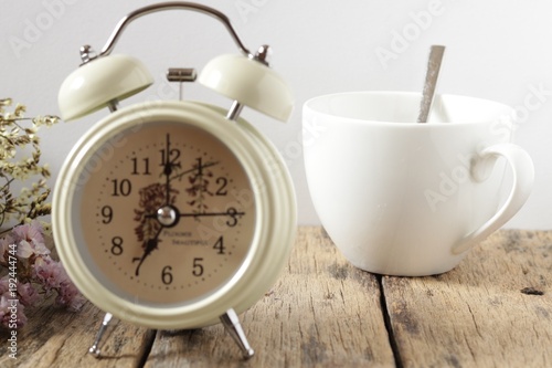 A white coffee cup with Alarm clock on the wood on white background, Vintage filter style, Vintage concept