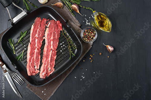 Canvas Print Bacon rashers on grill pan with rosemary, garlic and olive oil isolated on black background