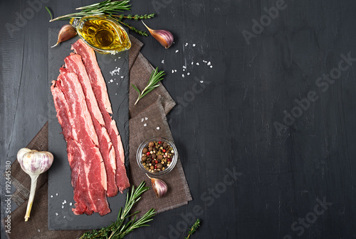 Fotografia Bacon rashers with rosemary, garlic and olive oil isolated on black background