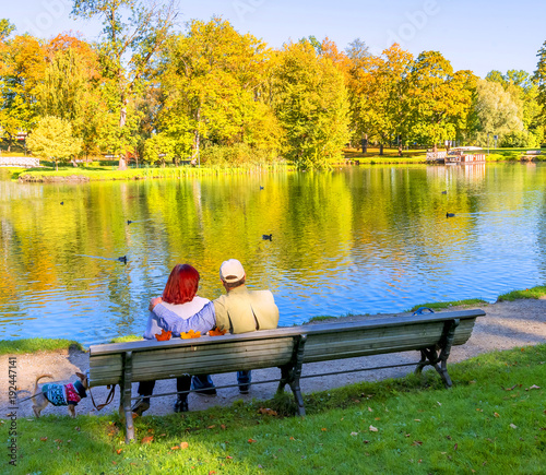 Happy couple of seniors are resting on the wooden bench in autumnal public ci...