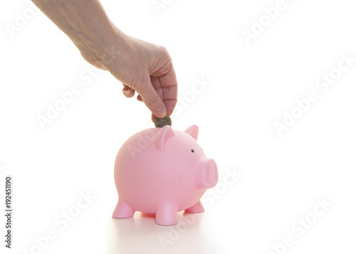 Female hand putting one euro coin in a a pink piggybank seen from the side on a white background