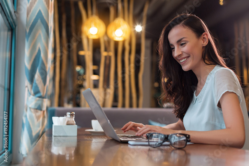 Work everywhere. Attractive beautiful female freelancer typing while looking at screen and smiling photo