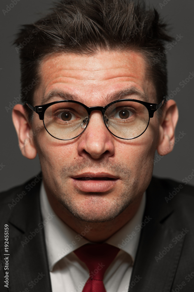 Close-up portrait of curious businessman in formal costume and wearing glasses on gray background