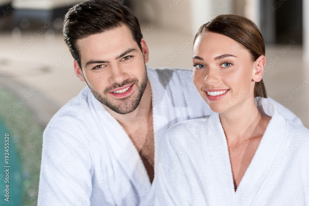 beautiful young couple in bathrobes smiling at camera in spa center beautiful young couple in bathrobes smiling at camera in spa center