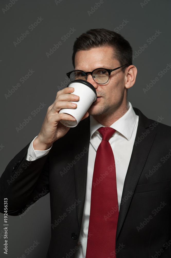 Portrait of handsome businessman wearing glasses and formal attire drinking coffee on gray background. Portrait of handsome businessman wearing glasses and formal attire drinking coffee on gray background.