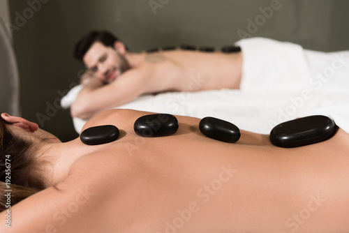cropped shot of couple looking at each other while having hot stones massage in spa center