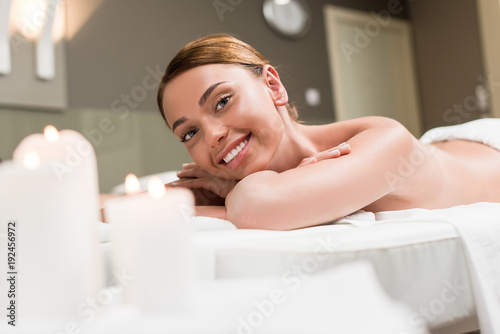 beautiful young woman smiling at camera while lying on massage table in spa salon
