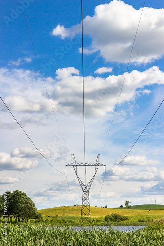 Power pylons and high voltage lines in the green grass field with blue sky and cloud photo