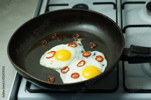 Two fried eggs with chili pepper in a skillet.