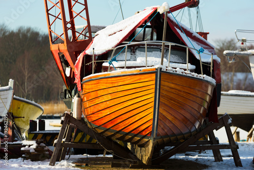 Fine wooden boat on land under a tarp at a marina for winter storage, seen from the fore or front. Logos and names removed. photo