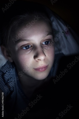 Girl Using Mobile Phone Hiding Under Duvet In Bed At Night