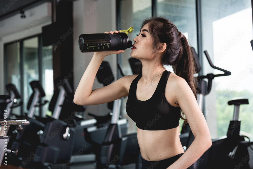 Sports young woman with protein cocktail in shaker sits in gym Sports young woman with protein cocktail in shaker sits in gym