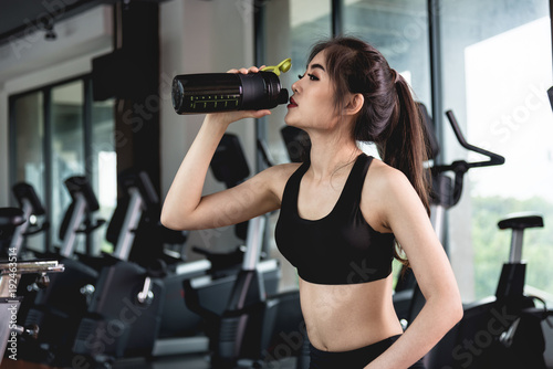 Sports young woman with protein cocktail in shaker sits in gym