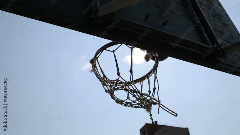 Ball going through broken basketball hoop during street game, physical activity Ball going through broken basketball hoop during street game, physical activity