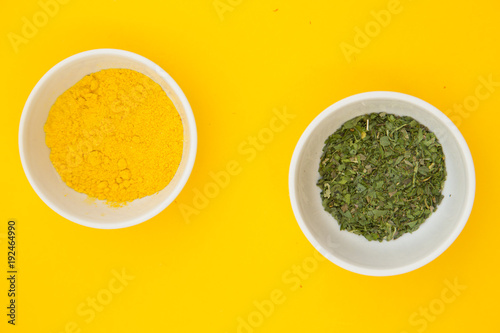 Plastic cups with dry spices and fresh herbs on a yellow background with copy space, top view, close up