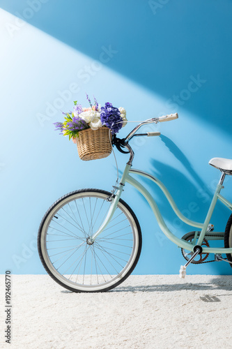bicycle with beautiful flowers in basket in front of blue wall
