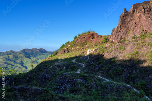 Dirt road in shadow of rock mountain with blue sky © oppdowngalon