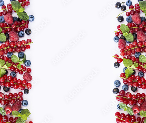 Berries at border of image with copy space for text. Top view. Ripe red currants, strawberries, raspberries, blackberries, blueberries and blackcurrants on white background.