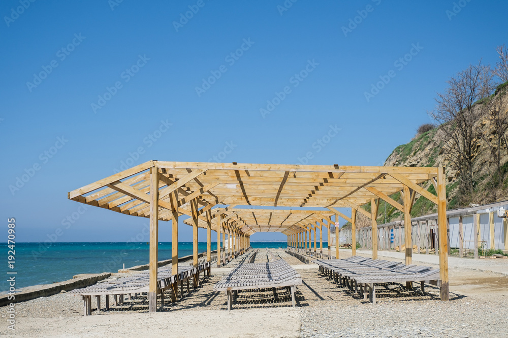 Wooden sun loungers on a pebbled public beach by the sea. Wooden sun loungers on a pebbled public beach by the sea.