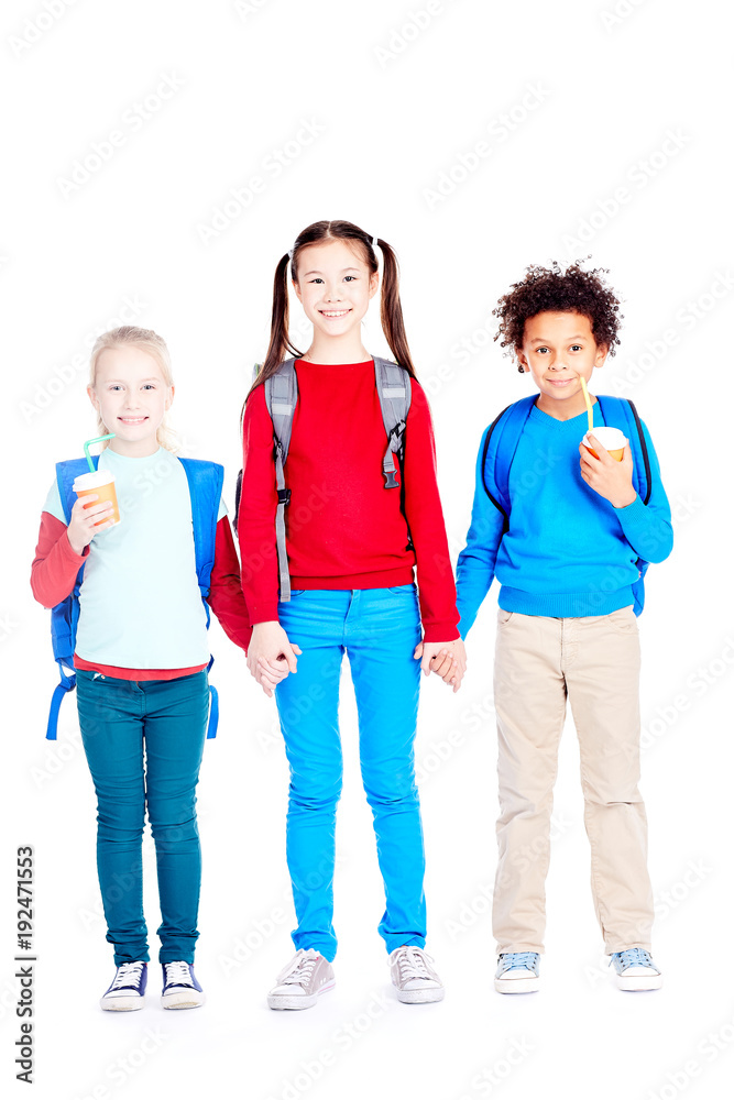Obraz premium Portrait of three multi-ethnic school friends holding hands on white background