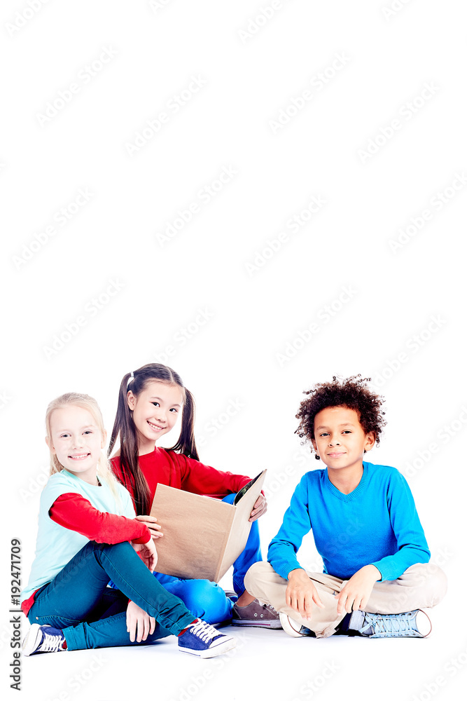 Three multi-ethnic elementary students sitting on floor and reading a book together